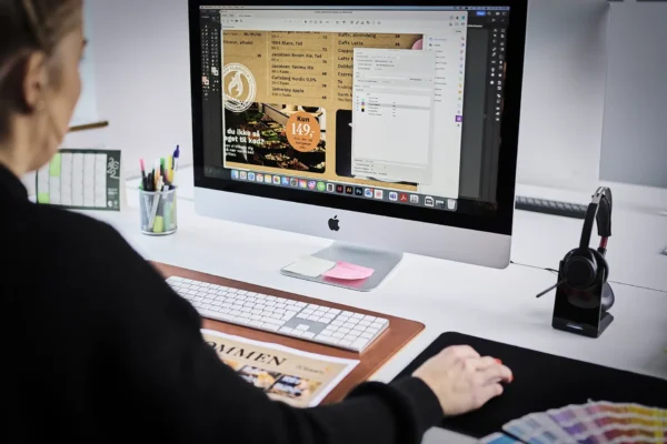 Grafisk designer arbejder foran sin iMac computer, laver design i InDesign